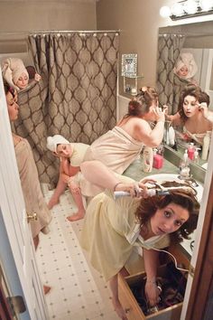 a woman in a bathrobe is looking at herself in the mirror while others are brushing her hair