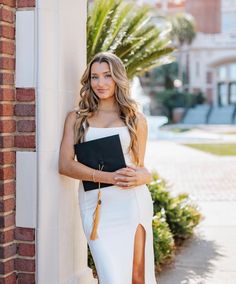 a woman leaning against a wall wearing a white dress and holding a black binder