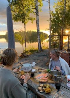 two women sitting at a picnic table with food on it and the sun setting in the background