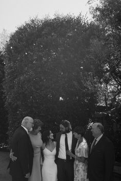 a group of people standing next to each other in front of a tree and bushes