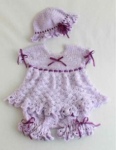 a crocheted baby dress and hat on a white sheet with purple trims