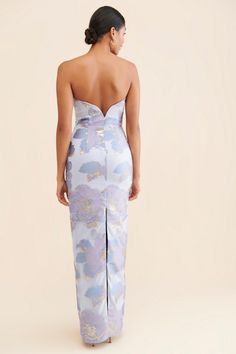 the back of a woman wearing a blue and white floral print dress with high slits