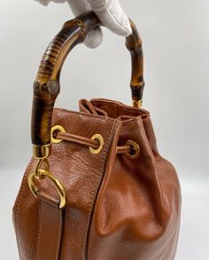 The cutest vintage brown/tan leather Gucci bucket bag with the iconic Gucci bamboo handles plus a leather crossbody strap. The crossbody strap can be taken off if you wish. This bag features gold Gucci branded hardware and gold feet on the base to protect the bag. Inside the lining is in excellent condition with a zipped interior pocket for valuables. The crossbody strap drop is 40cm. Gucci first introduced the bamboo handle in 1947 following a leather shortage as a result of the war, forcing craftspeople to experiment and look for new materials. The bamboo handles are extremely durable and a classic now for the house. This bag is in excellent vintage condition, inside the bag is immaculate., it hardly has been used. Gucci Bucket Bag, Gucci Brand, Bag Inside, Gucci Bamboo, Bamboo Handles, Vuitton Bag, Diaper Backpack, Exclusive Bag, Casual Backpack