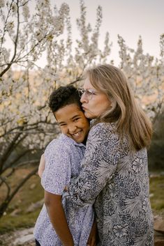 an older woman and young boy embracing each other in front of blooming apple trees