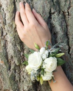 a woman's hand holding onto a white flower bouquet on a tree trunk,