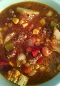 a bowl of soup with meat, beans and vegetables in it sitting on a table