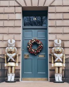 two gold nutcrackers stand in front of a blue door with a wreath on it