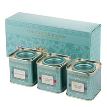 three tea tins sitting next to each other in front of a box with labels on them