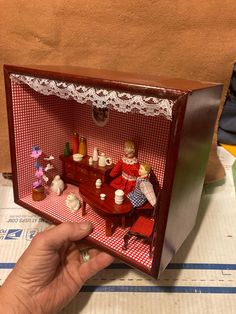 a hand holding a miniature doll house with furniture and accessories in the box on the table