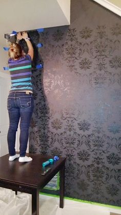 a woman standing on top of a table in front of a wallpapered room