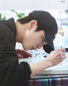 a young man wearing a hat looking at something on a laptop computer while leaning over his head