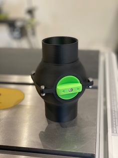 a black and green vase sitting on top of a metal counter next to a yellow object