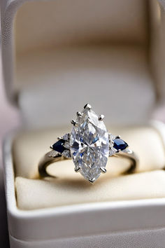 an oval cut diamond with blue accents sits in a white velvet ring box on display