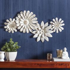 three white flowers on a blue wall next to a potted plant and candle holder