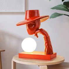 an orange sculpture with a red hat on it's head sitting on a table