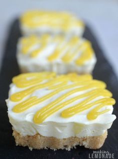 three desserts with white and yellow icing sitting on a black plate next to each other