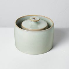 a white ceramic container with a lid on a plain table top, next to a wall