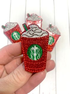 a hand holding a red sequined starbucks pin with four cups on it and one cup in the middle