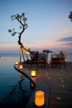 candles lit up on the edge of a pool at dusk with an outdoor dining area in the background