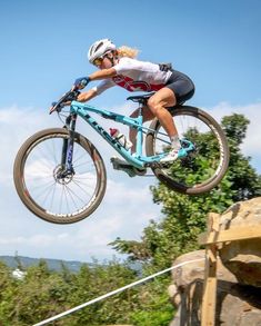 a person on a bike jumping in the air over some rocks and grass with trees behind them