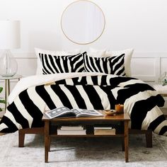 a zebra print comforter on a bed in a white room with a round mirror