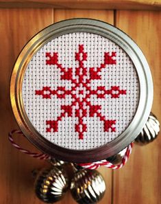 a cross stitch ornament hanging from a metal can with bells on the side