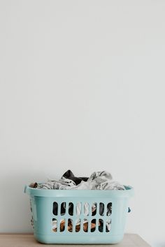 a blue laundry basket sitting on top of a wooden table next to a white wall