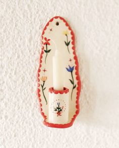 a white candle is sitting on a red and white plate with flowers painted on it