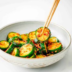 a white bowl filled with cucumbers and topped with chopsticks