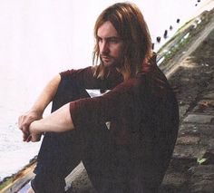 a man with long hair sitting on the ground