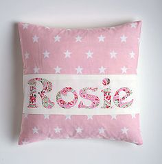 a pink pillow with white stars and the word rose on it, sitting against a wall