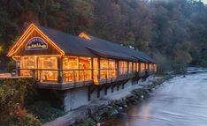 a restaurant on the side of a river at dusk with its lights on and windows lit up