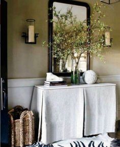 a table with a white cloth on it in front of a mirror and vase filled with flowers