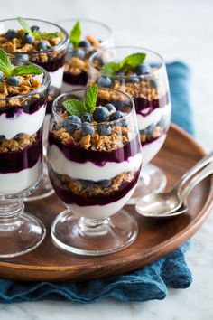 three desserts with blueberries and yogurt are on a wooden platter