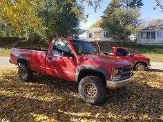 a red pick up truck parked on top of leaf covered ground in front of a house