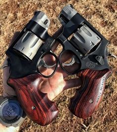 a person holding two revolvers in their hand on the ground with grass behind them