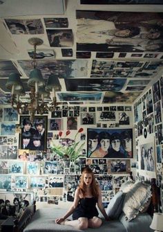 a woman sitting on top of a bed in a room filled with pictures and photos