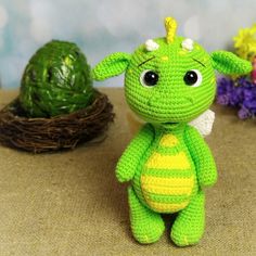 a crocheted green and yellow stuffed animal sitting next to an easter egg in a nest