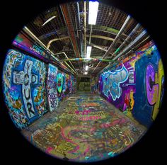 a tunnel with graffiti all over the walls and floor is shown through a fish eye lens