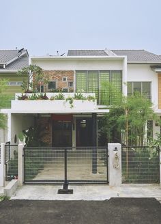 a white house with black gate and plants on the top floor, in front of it