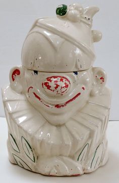 a white ceramic clown face jar with red and green paint on it's head