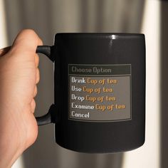 a person holding a black coffee mug with the words drink cup of tea on it