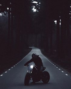 a man riding on the back of a motorcycle down a dark road in the woods