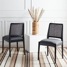 two chairs sitting next to each other on top of a striped rug in front of a white wall