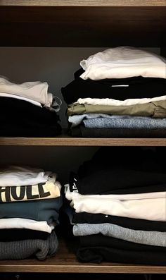 an open closet with clothes on the shelves and folded shirts in front of it,