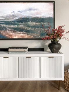 a vase with flowers sitting on top of a white cabinet in front of a painting