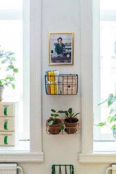 two plants are hanging on the wall next to some boxes and baskets with books in them