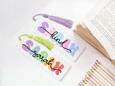 two name tags with tassels and colored pencils next to an open book