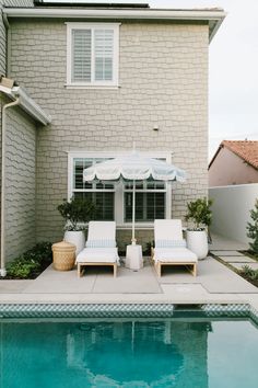 two lounge chairs sitting next to a swimming pool in front of a brick building with a white awning over it