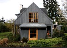 a gray house with a metal roof and two windows on the top floor is surrounded by greenery